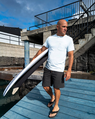 Kelly Slater wearing Outerknown UPF 50 sun shirt walking with Surfboards.