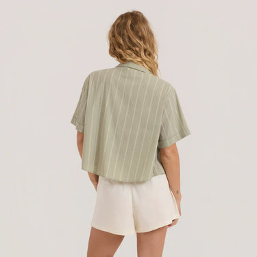 Person wearing a green striped shirt and white shorts on a plain background
