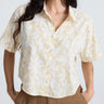 Woman wearing a beige and white patterned shirt against a white background