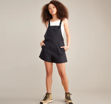 Person wearing black overalls and hiking boots on a plain background