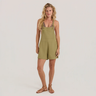 A woman modeling a sage green sleeveless bib romper with shoulder straps and short legs, paired with tan flat sandals, against a light gray studio background.