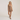A woman modeling a brown overall-style romper dress with shoulder straps and a square neckline, photographed against a plain light beige studio background.