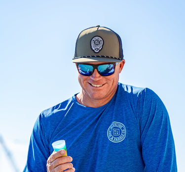 Man wearing the olive and black Skully rope hat from Blueline Surf & Paddle Co. while boating in Jupiter Florida, featuring custom skull artwork and coastal saltwater lifestyle styling.