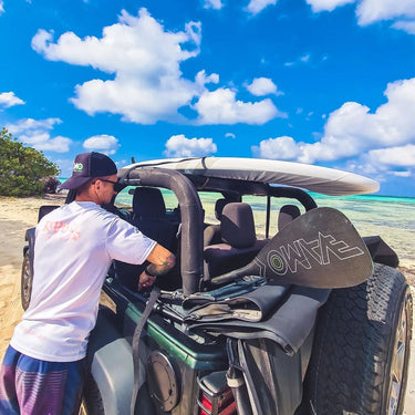 A waterman loads a Vamo SR71 full carbon fiber performance paddle into a Jeep Wrangler at the Jupiter Florida beach, with a paddleboard and pristine ocean background