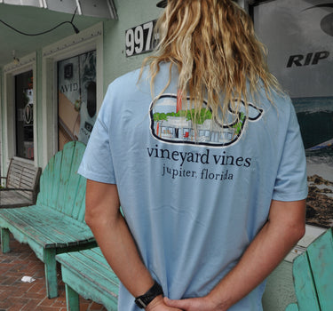 Back view of a person wearing a Jake Blue Vineyard Vines x Blueline t-shirt with a vintage storefront lighthouse graphic and Jupiter, Florida text.