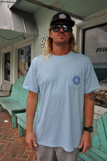 Person wearing a blue Vineyard Vines and Blueline shirt with a front pocket logo, standing in front of Blueline Surf and Paddle in Jupiter, Florida