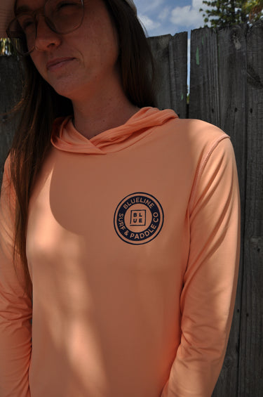 Woman wearing the Women’s OG Logo Hooded UV Sun Shirt Coral from Blueline Surf & Paddle Co. designed for sun protection, boating, beach days, paddling, and coastal outdoor adventures.